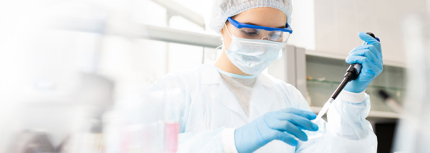 Eine Laborchemikerin mit Schutzbrille, Mundschutz und Haube nimmt eine Probe ab.